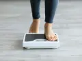 Pieds nus sur une balance, une personne s'interroge sur sa perte de poids inexpliquée.