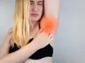 Une femme blonde exprime une douleur vive à l'aisselle, se tenant le bras avec une expression de souffrance.
