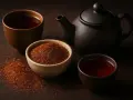 Découvrez le rooibos : une théière et des tasses de thé rouge ambré, avec un bol de feuilles de rooibos séchées.