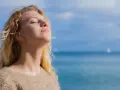 Jeune femme blonde profitant du soleil, source naturelle de vitamine D2 et D3, avec la mer en arrière-plan.
