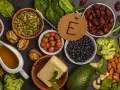 Assortiment d'aliments riches en vitamine E : amandes, noisettes, épinards, avocat, haricots noirs, graines de courge, et huile.