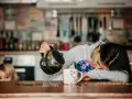 Une femme, accablée par la fatigue musculaire, verse du café dans une tasse. Un enfant la regarde, curieux.