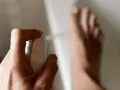 Main d'une personne pulvérisant un produit sur ses pieds, un remède de grand-mère contre la transpiration des pieds.