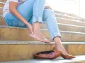 Douleur au talon ? Une femme s'assoit sur des marches, massant son pied. Peut-être un remède de grand-mère pour soulager cette gêne.