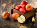 Des pommes rouges et jaunes dans une caisse en bois sur une table rustique. Une pomme est coupée en deux, révélant sa chair blanche. Ces fruits sont un concentré de pomme bienfaits.
