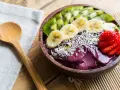 Un bol de smoothie aux fruits d'açaï, garni de bananes, de kiwis, de fraises et de graines.