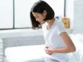 Jeune femme assise sur un lit, se tenant le ventre, souffrant de spasmes intestinaux.
