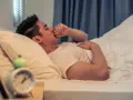 Un homme se réveille en pleine nuit, la main sur la bouche, pris d'une toux nocturne. L'horloge sur la table de nuit indique qu'il est 3h du matin.