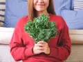 Une femme souriante tient un bouquet de chou kale, un légume aux multiples chou kale bienfaits pour la santé.