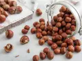 Des noisettes bienfaits : une poignée de ces fruits secs, certains dans un bocal renversé, d'autres sur une planche en bois, promettent une alimentation saine.