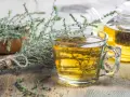 Une tasse de tisane thym digestion, avec du thym frais à côté et une théière en arrière-plan.