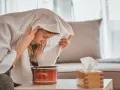 Jeune femme enroulée dans une serviette, profitant d'une inhalation vapeur pour soulager son rhume. Un pot rouge et une boîte de mouchoirs sont à proximité.