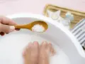 Une cuillère en bois déverse des cristaux dans un bain de pied, pour un moment de détente et de soin.