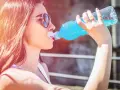 Une jeune femme aux lunettes de soleil boit une boisson bleue rafraîchissante, peut-être de l'eau de Quinton, sous le soleil.