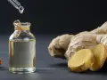 Goutte d'huile essentielle de gingembre aphrodisiaque tombant dans un flacon, à côté de racines de gingembre fraîches.