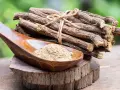 Racines de réglisse séchées et poudre de réglisse dans une cuillère en bois, évoquant les nombreux bienfaits de la réglisse.