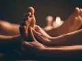 Mains massant un pied, avec des bougies allumées en arrière-plan.