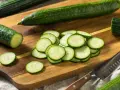 Concombres frais tranchés sur une planche à découper en bois, prêts à révéler leurs nombreux concombre bienfaits. Un couteau est à proximité.