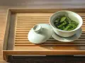 Une tasse de thé vert infusé, prête à révéler ses bienfaits. Le couvercle repose à côté, sur un plateau en bambou.