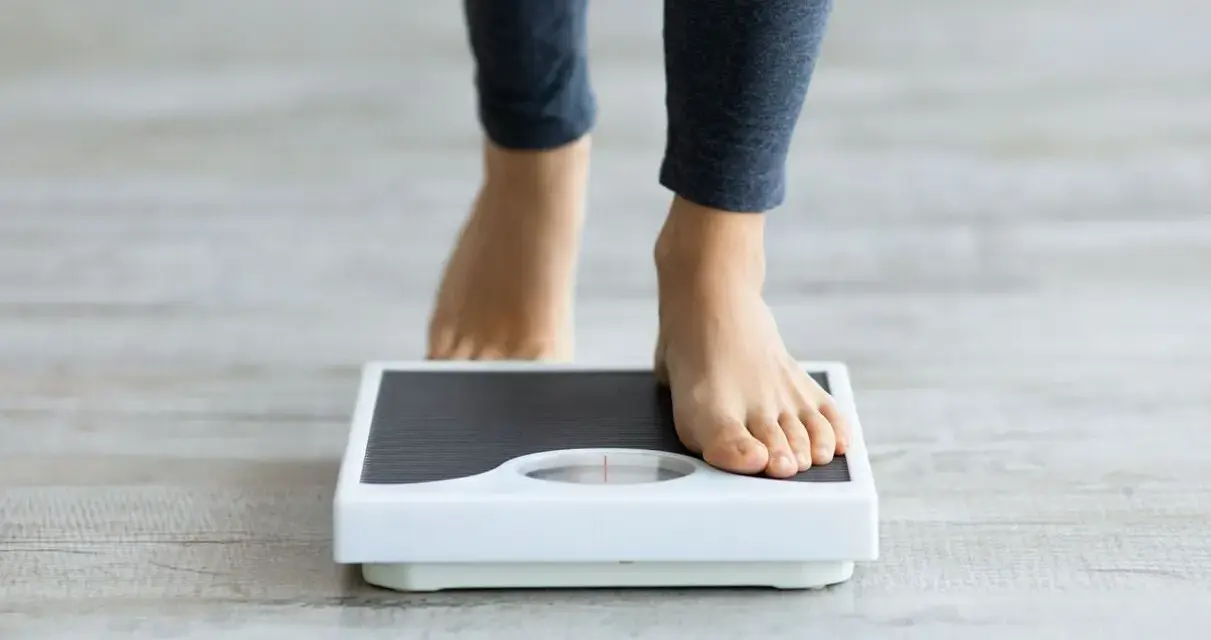 Pieds nus sur une balance, une personne s'interroge sur sa perte de poids inexpliquée.