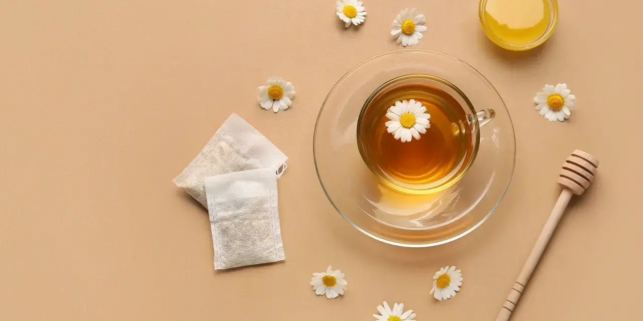 Une tasse de tisane pour le rhume et la toux, avec des sachets, du miel et des fleurs de camomille.