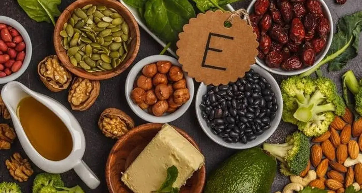 Assortiment d'aliments riches en vitamine E : amandes, noisettes, épinards, avocat, haricots noirs, graines de courge, et huile.