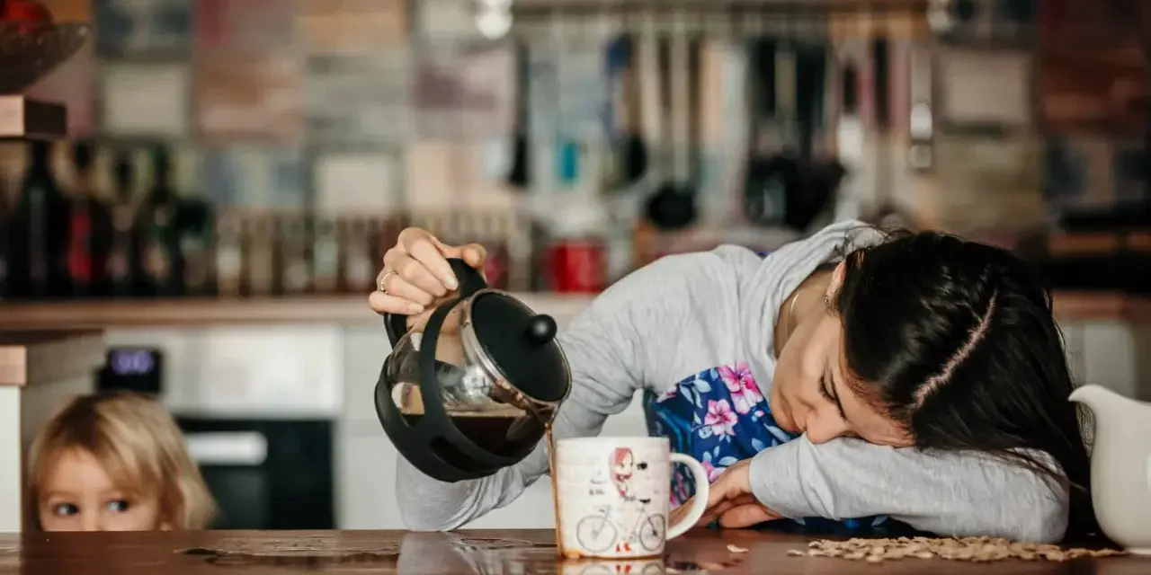 Une femme, accablée par la fatigue musculaire, verse du café dans une tasse. Un enfant la regarde, curieux.