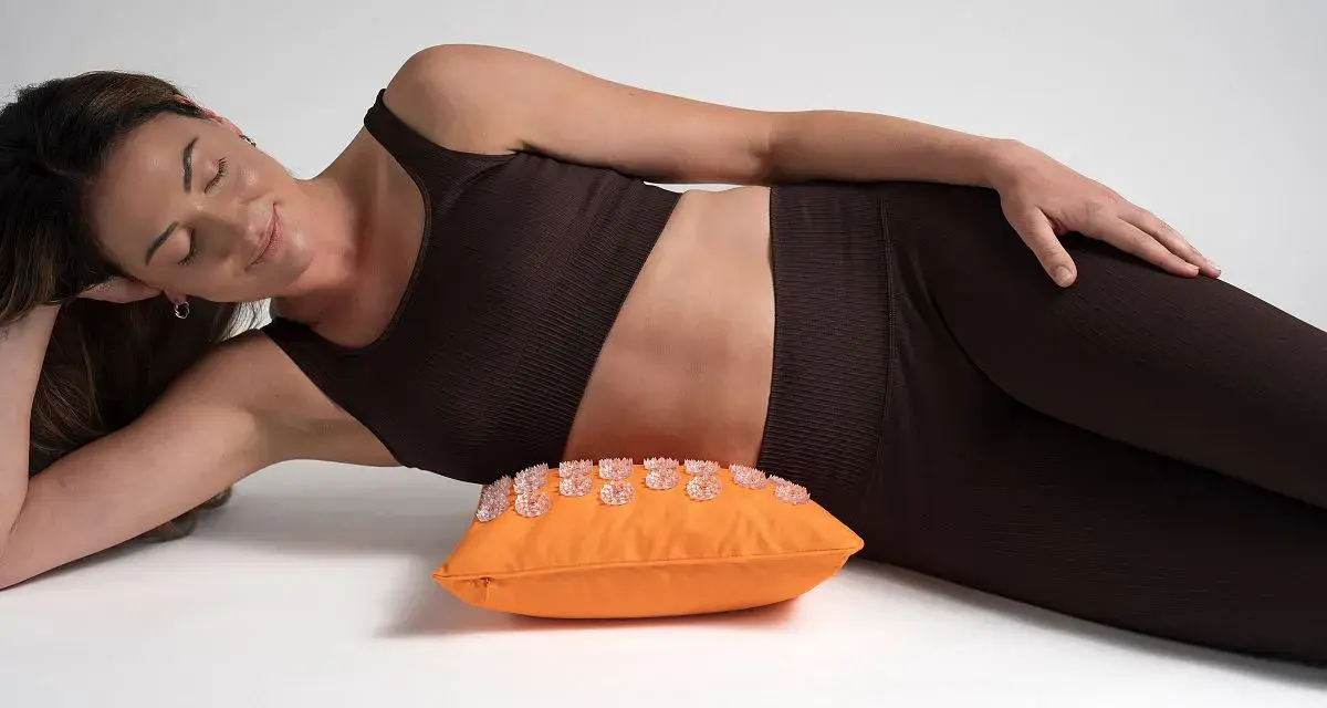 Femme détendue sur un coussin d'acupression orange, une solution pour le mal de hanche que faire.