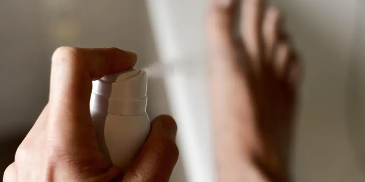 Main d'une personne pulvérisant un produit sur ses pieds, un remède de grand-mère contre la transpiration des pieds.