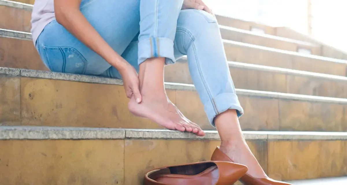Douleur au talon ? Une femme s'assoit sur des marches, massant son pied. Peut-être un remède de grand-mère pour soulager cette gêne.
