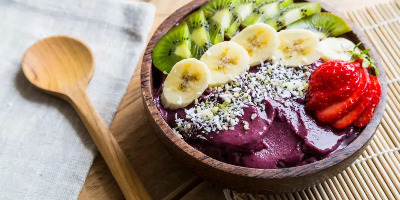 Un bol de smoothie aux fruits d'açaï, garni de bananes, de kiwis, de fraises et de graines.