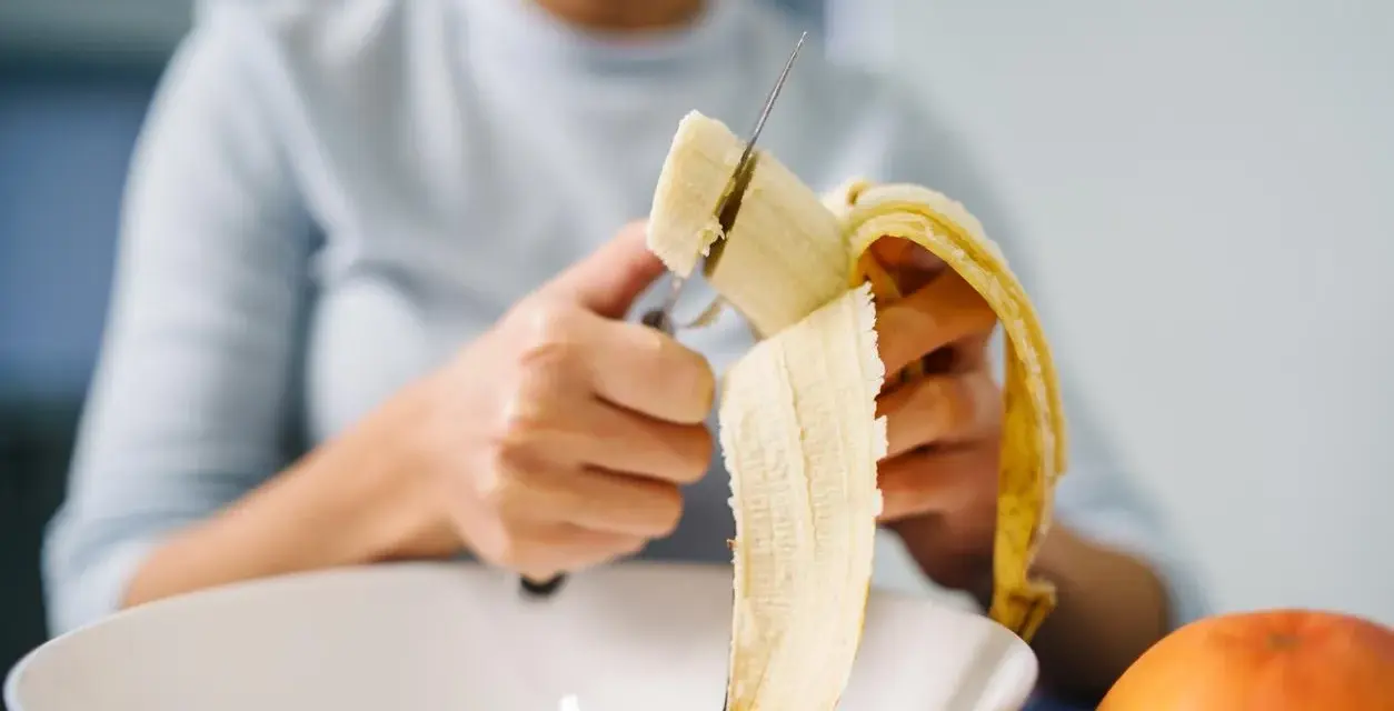 Une personne coupe une banane, riche en potassium, pour prendre soin de son cœur.