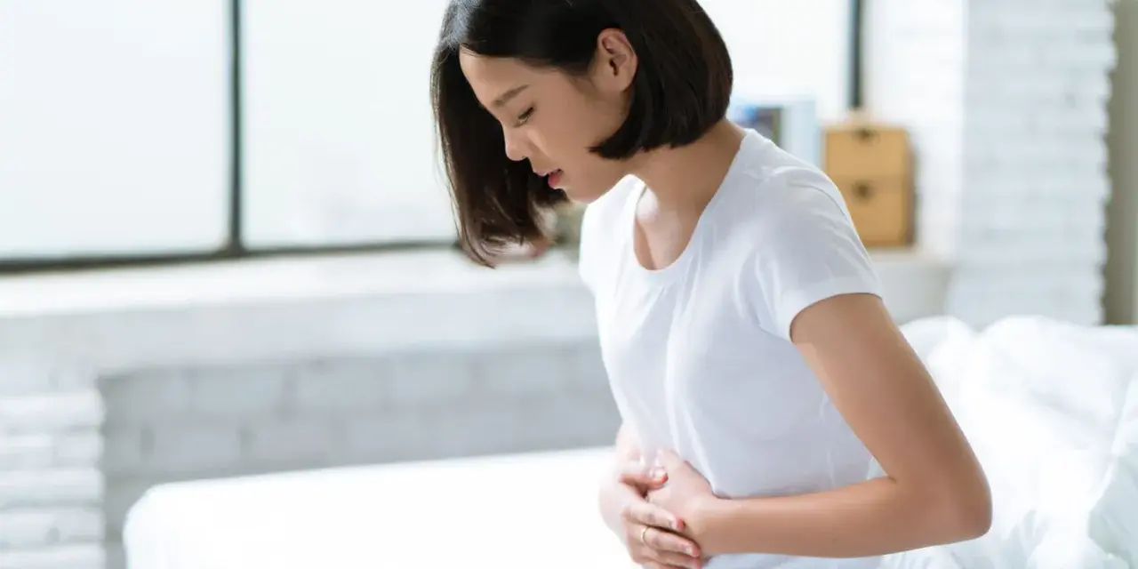 Jeune femme assise sur un lit, se tenant le ventre, souffrant de spasmes intestinaux.