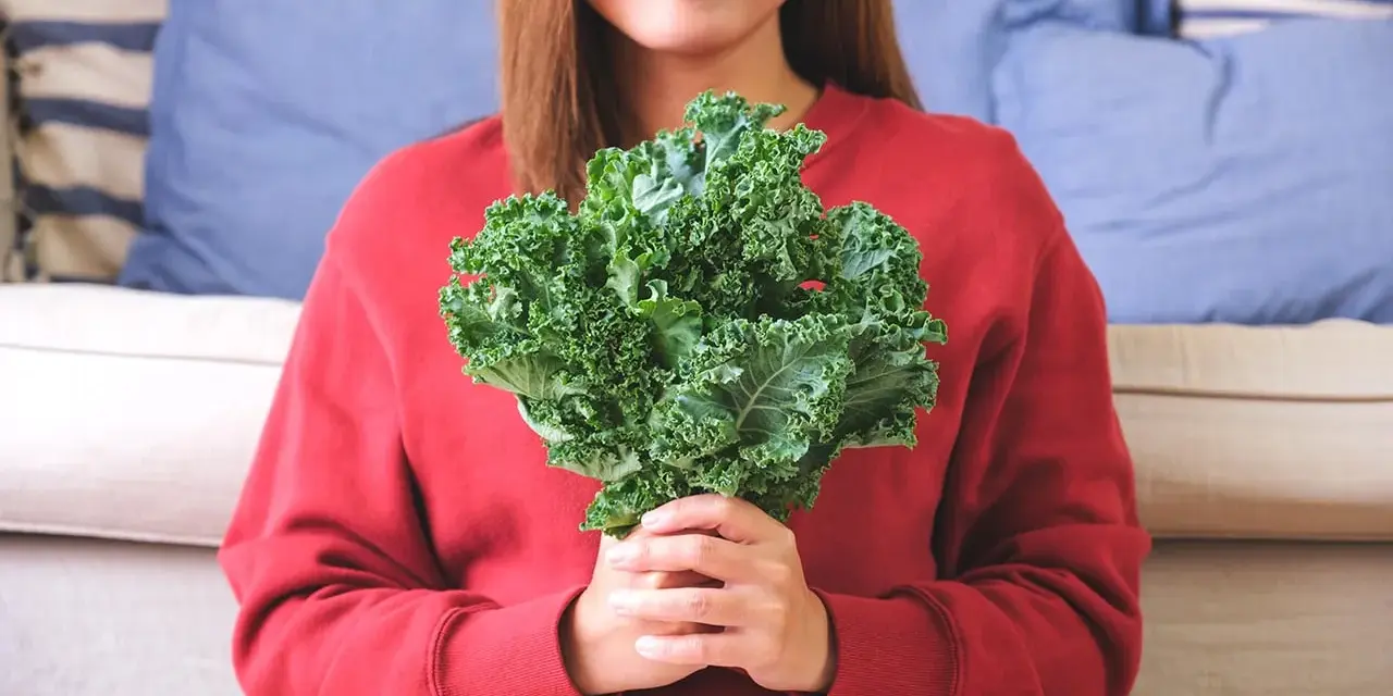 Une femme souriante tient un bouquet de chou kale, un légume aux multiples chou kale bienfaits pour la santé.