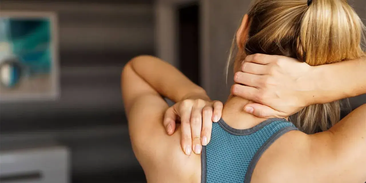 Une femme se masse le cou, cherchant un remède de grand-mère pour sa douleur cervicale.