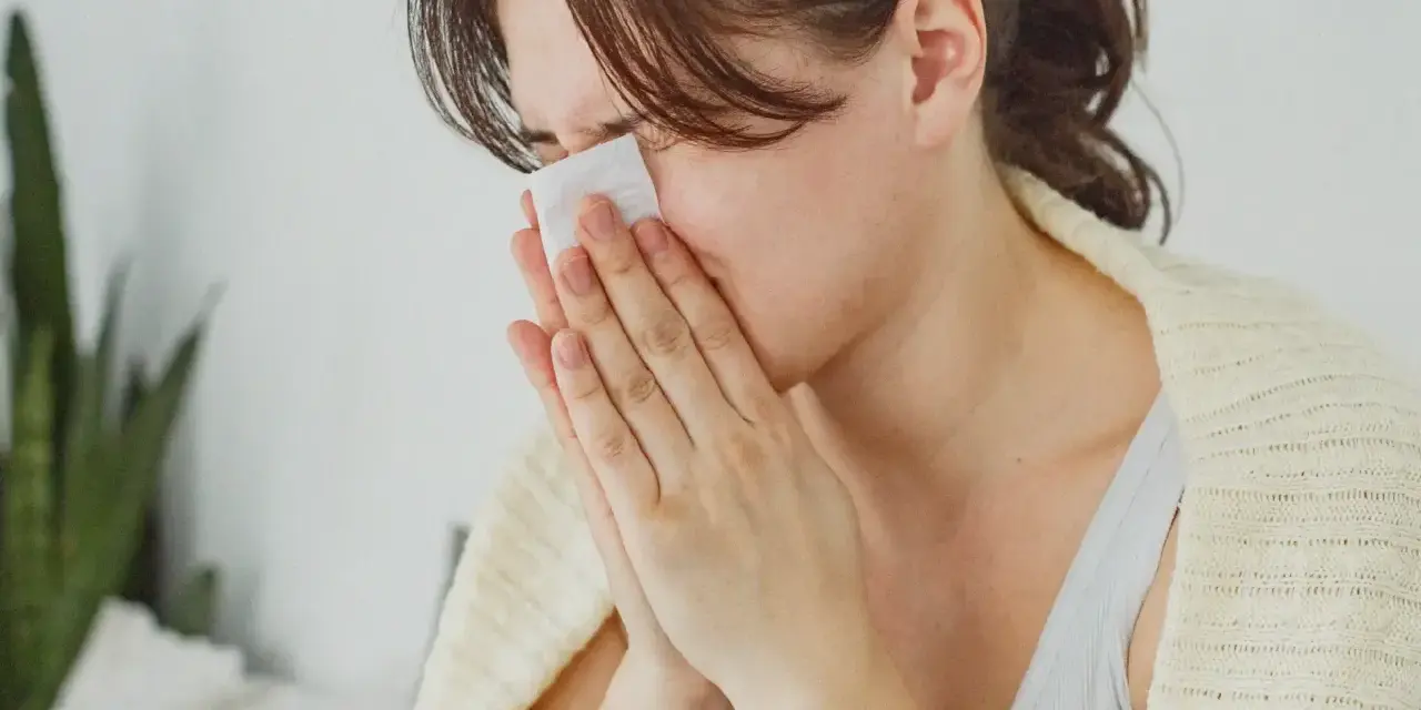 Femme se mouchant avec un mouchoir, cherchant des solutions pour comment arrêter le nez qui coule naturellement.