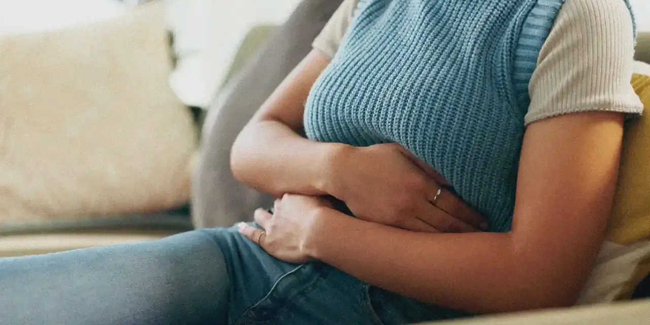 Une personne assise sur un canapé, tenant son abdomen, suggérant où se situe une douleur au foie.
