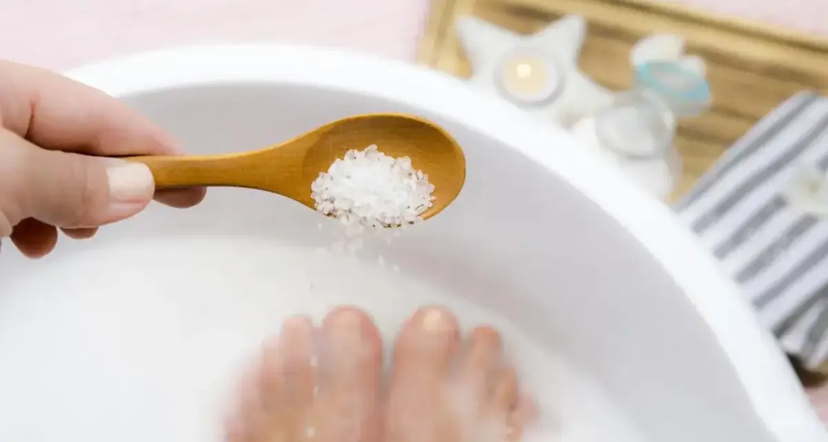 Une cuillère en bois déverse des cristaux dans un bain de pied, pour un moment de détente et de soin.