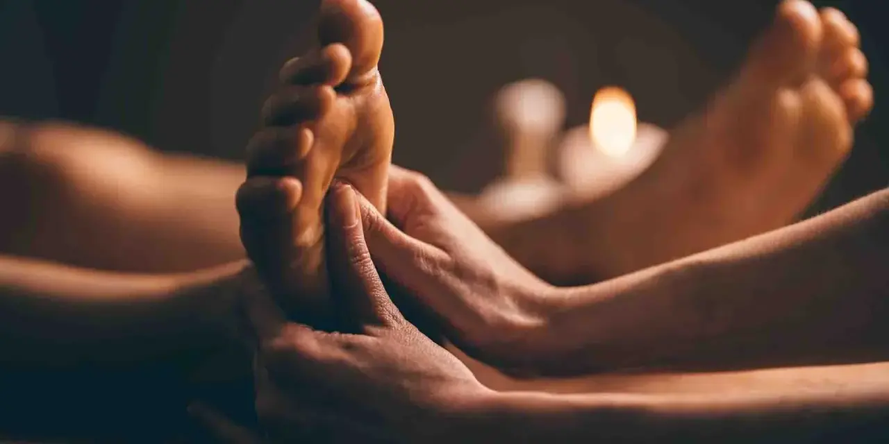 Mains massant un pied, avec des bougies allumées en arrière-plan.