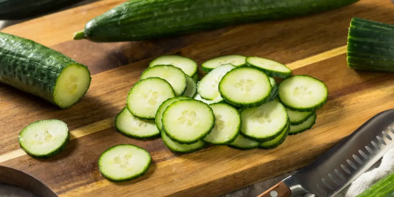 Concombres frais tranchés sur une planche à découper en bois, prêts à révéler leurs nombreux concombre bienfaits. Un couteau est à proximité.
