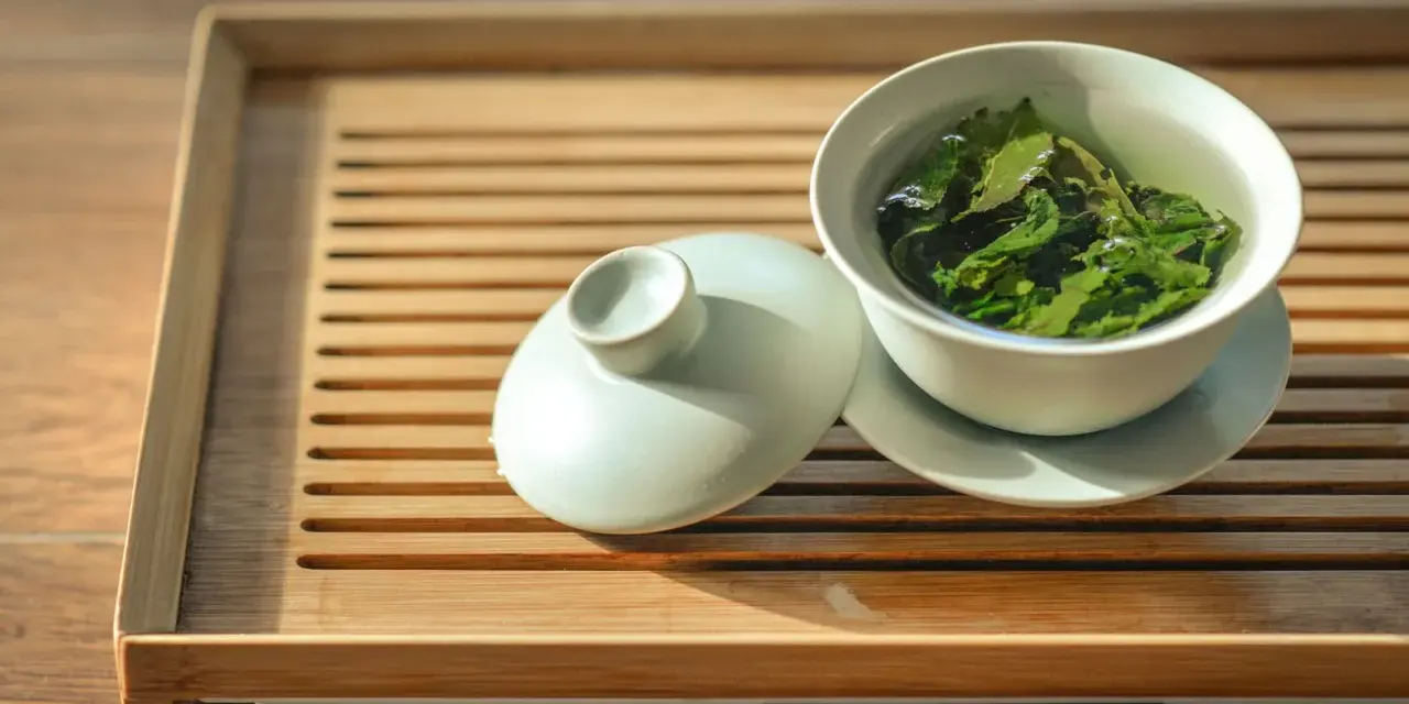 Une tasse de thé vert infusé, prête à révéler ses bienfaits. Le couvercle repose à côté, sur un plateau en bambou.