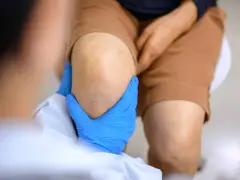 Main bleue examinant un genou, suggérant une approche de traitement naturel pour l'arthrose du genou.