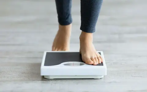 Pieds nus sur une balance, une personne s'interroge sur sa perte de poids inexpliquée.
