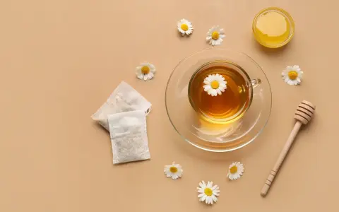Une tasse de tisane pour le rhume et la toux, avec des sachets, du miel et des fleurs de camomille.