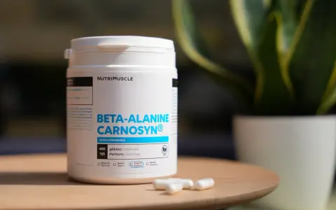 Bouteille de bêta-alanine Carnosyn® pour l'endurance musculaire, avec des capsules sur une table en bois.