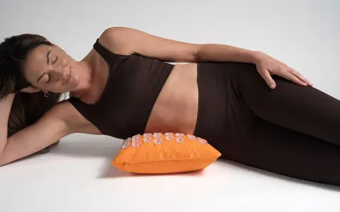 Femme détendue sur un coussin d'acupression orange, une solution pour le mal de hanche que faire.