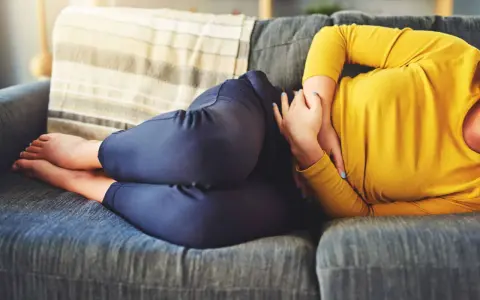 Femme enroulée sur un canapé, se tenant le ventre. Elle se demande combien de temps dure une gastro.