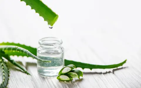 Goutte de gel d'aloe vera tombant dans un petit flacon, entouré de feuilles d'aloe vera coupées.