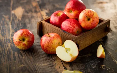 Des pommes rouges et jaunes dans une caisse en bois sur une table rustique. Une pomme est coupée en deux, révélant sa chair blanche. Ces fruits sont un concentré de pomme bienfaits.