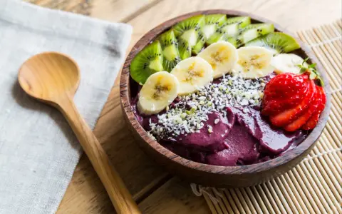 Un bol de smoothie aux fruits d'açaï, garni de bananes, de kiwis, de fraises et de graines.